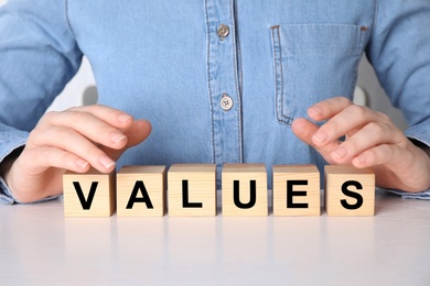 Photo of Core values concept. Woman with cubes at wooden table, closeup
