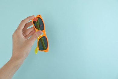 Woman holding stylish sunglasses on light blue background, closeup. Space for text