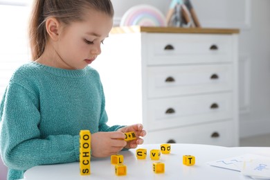 Little girl assembling word with yellow bricks in classroom at English lesson