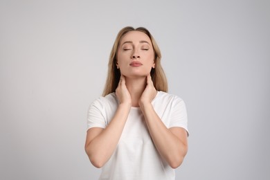 Young woman doing thyroid self examination on light grey background