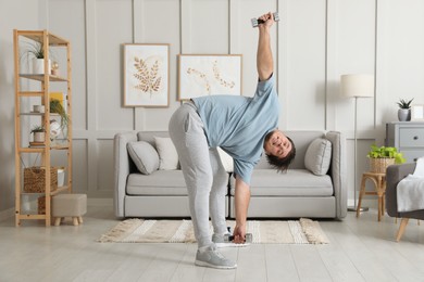 Overweight man doing exercise with dumbbells at home