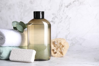 Shampoo bottle, loofah, folded towels and pumice on white marble table, space for text