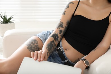 Beautiful woman with tattoos on body using laptop in living room, closeup