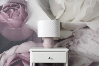 White nightstand near wall with floral wallpaper. Stylish room interior