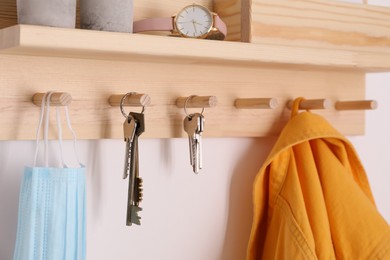 Wooden hanger for keys with different stuff on white wall, closeup