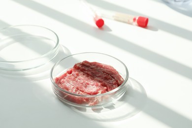 Photo of Petri dish with pieces of raw cultured meat on white table in laboratory, space for text