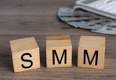 Cubes with abbreviation SMM (Social media marketing), money and calculator on wooden table