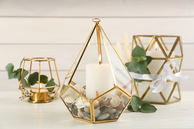 Stylish glass holders with burning candles and beautiful decor on white wooden table