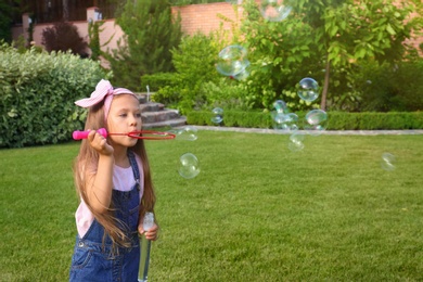 Cute little girl blowing soap bubbles in green park