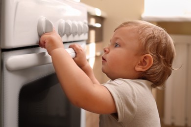 Photo of Little child playing with gas stove indoors. Dangers in kitchen