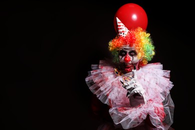 Photo of Terrifying clown with red air balloon on black background, space for text. Halloween party costume