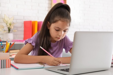 Photo of Pretty preteen girl doing homework with laptop at table