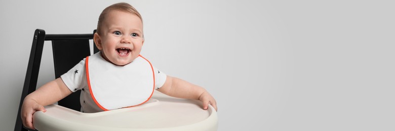 Image of Cute little baby wearing bib in highchair on white background, space for text. Banner design