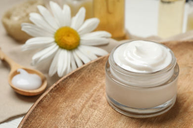 Cosmetic cream and chamomile on table, closeup