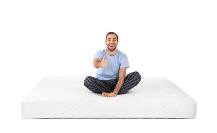 Young man sitting on mattress against white background