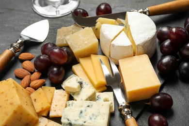 Cheese platter with specialized knives and fork on black table, closeup view