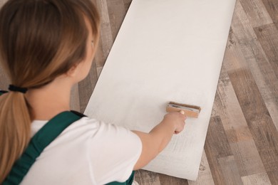 Worker applying glue onto wall paper sheet, focus on hand