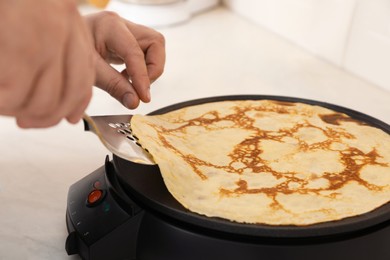Man cooking delicious crepe on electric pancake maker in kitchen, closeup