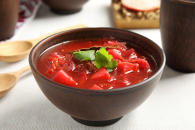 Stylish brown clay bowl with Ukrainian borsch served on white tablecloth, closeup