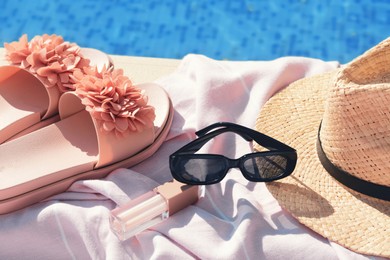 Photo of Pink blanket with beach accessories near outdoor swimming pool on sunny day, closeup