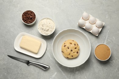 Photo of Fresh dough and different ingredients for cooking chocolate chip cookies on light grey marble table, flat lay