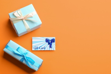 Gift card and presents on orange background, flat lay. Space for text