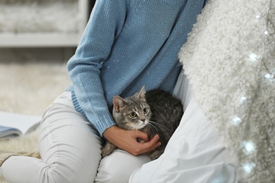 Young woman with cute cat at home, closeup. Cozy winter