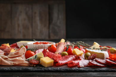 Photo of Tasty prosciutto with other delicacies served on black table