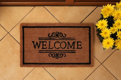 Door mat with word Welcome and beautiful flowers on floor, flat lay