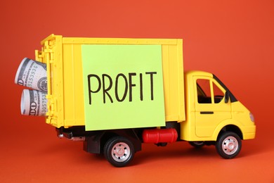 Economic profit concept. Toy truck with banknotes on red background