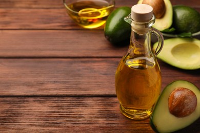 Photo of Glass bottle of cooking oil and fresh avocados on wooden table, closeup. Space for text