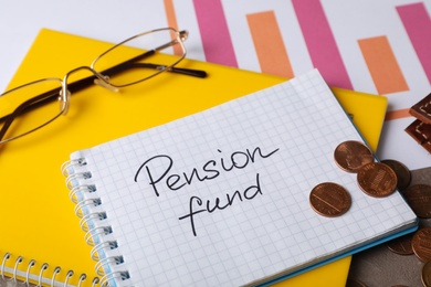 Coins, glasses and notebook with words PENSION FUND on table