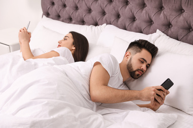 Young couple addicted to smartphones in bed at home