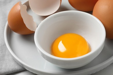 Chicken eggs and bowl with raw yolk on table, closeup