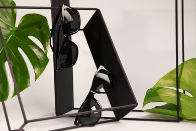 Stylish sunglasses hanging on black shelf against white background