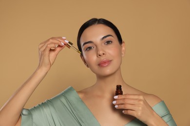 Young woman applying essential oil onto face against beige background