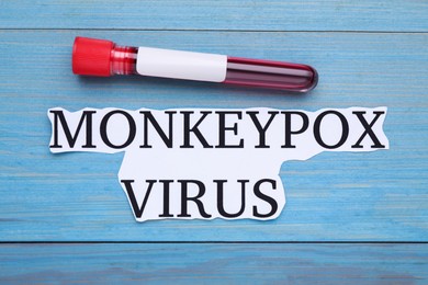 Photo of Card with words Monkeypox Virus and test tube on light blue wooden table, flat lay