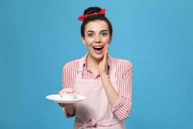 Young housewife with tasty cupcake on light blue background