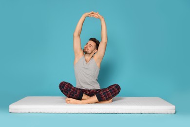 Man stretching on soft mattress against light blue background