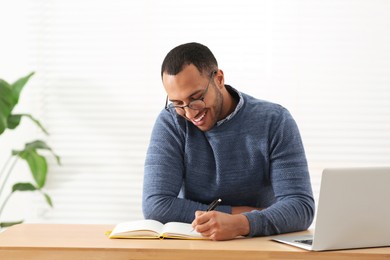 Photo of Smiling African American man writing in notebook at wooden table