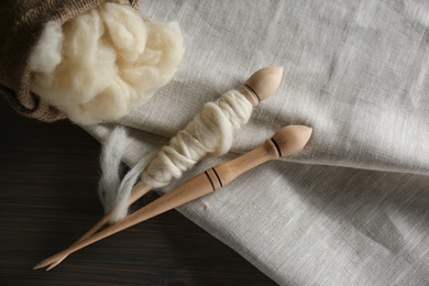 Soft white wool, spindles and fabric on wooden table, flat lay