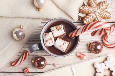 Flat lay composition with cup of tasty cocoa and Christmas candy canes on white wooden table, flat lay
