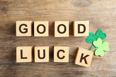 Cubes with phrase GOOD LUCK and clover leaves on wooden background, flat lay
