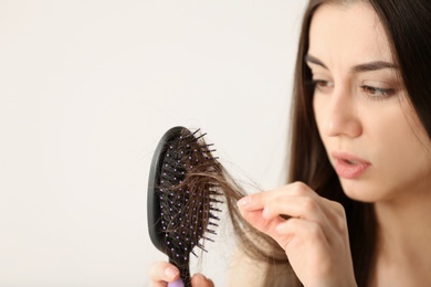 Photo of Woman untangling her hair from brush on light background. Space for text