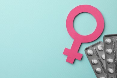 Female gender sign, blisters of pills and space for text on turquoise background, flat lay. Women's health concept