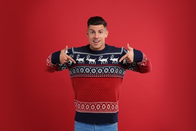Handsome man pointing on his Christmas sweater against red background
