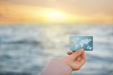 Woman holding credit card against sea, closeup view