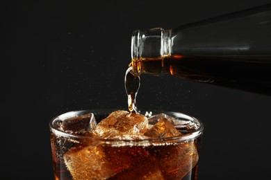 Pouring refreshing soda water from bottle into glass on black background, closeup