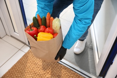 Courier holding paper bag with food in doorway, closeup. Delivery service during quarantine due to Covid-19 outbreak