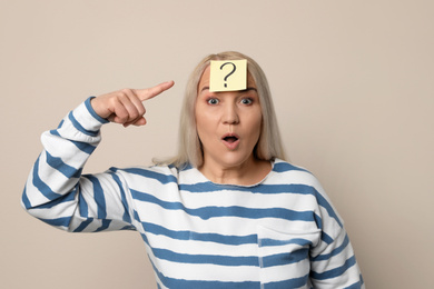 Emotional mature woman with question mark on beige background